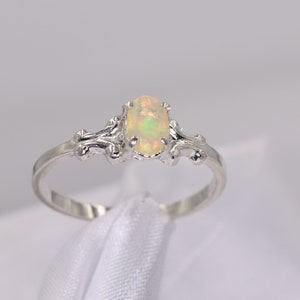 Puede incluir: Un anillo de plata con una piedra de ópalo ovalada. El anillo tiene un diseño delicado y adornado con espirales y curvas.