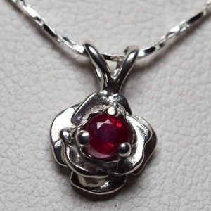 May include: A silver necklace with a rose-shaped pendant featuring a red ruby gemstone.