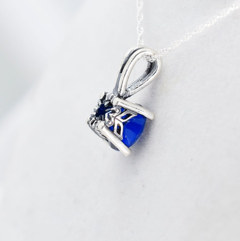 May include: A silver pendant necklace with a blue gemstone set in a detailed silver frame. The pendant is attached to a silver chain.