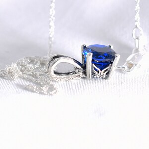 May include: A silver necklace with a blue gemstone pendant. The pendant has a detailed design and a round, faceted stone.