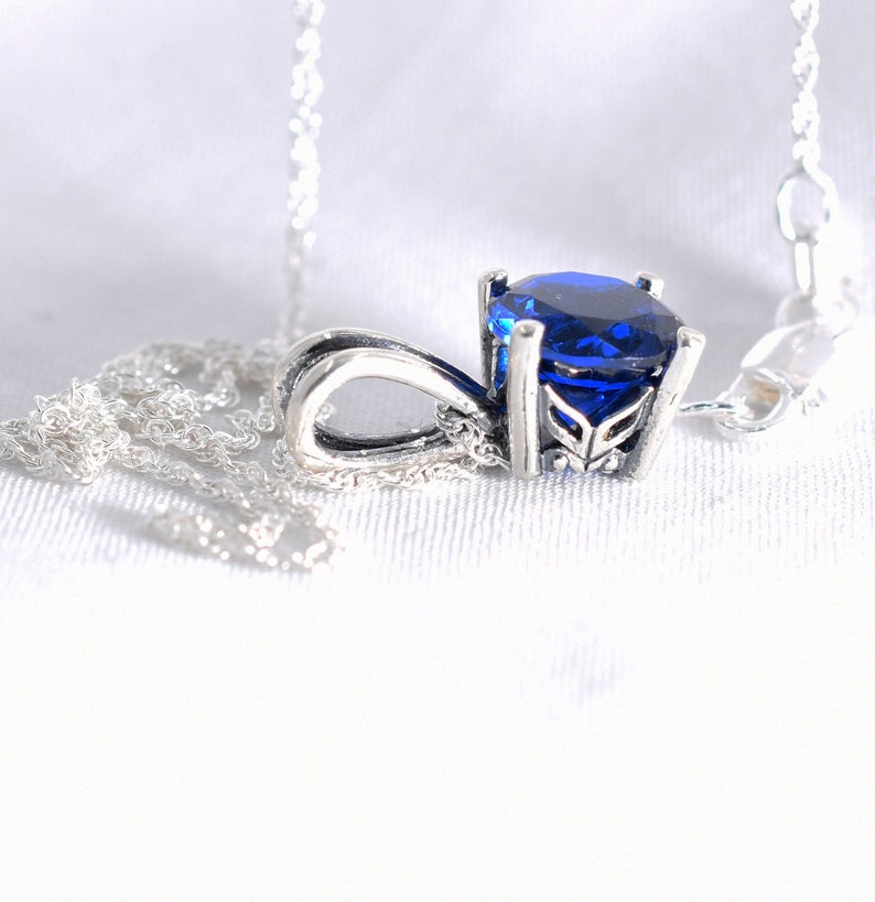 May include: A silver necklace with a blue gemstone pendant. The pendant has a detailed design and a round, faceted stone.