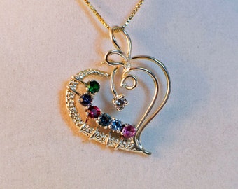 May include: A gold heart-shaped pendant necklace with a delicate swirl design. The pendant features a row of colorful gemstones, including green, blue, purple, red, and pink.