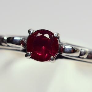 May include: A silver ring with a deep red ruby gemstone set in a four-prong setting.