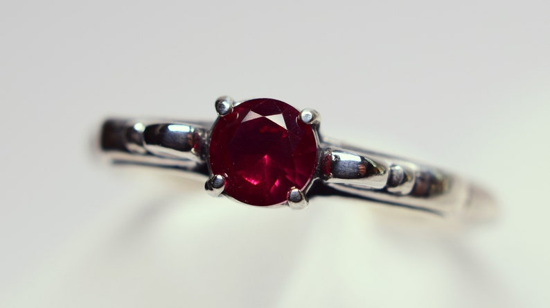 Puede incluir: Un anillo de plata con una piedra preciosa de rub&iacute; rojo oscuro engastada en un engaste de cuatro garras.