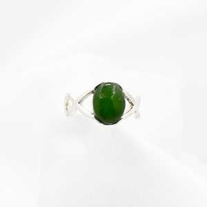 May include: A silver ring with a green oval gemstone set in a Celtic knot design.