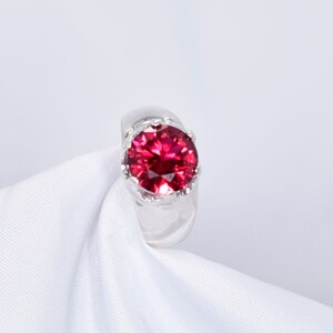 May include: A silver ring with a large, round, red gemstone set in a crown-like design.