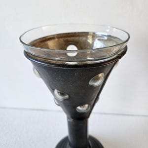May include: A decorative, antique-style glass and metal candle holder. The clear glass bowl sits atop a dark, cone-shaped metal base with clear glass bubble accents. The base is supported by a round, pedestal-style foot.