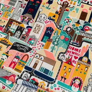 May include: A colorful fabric with a whimsical design featuring houses, trees, and other buildings. The fabric has a white background with black outlines and bright colors. The text "Home is where the heart is" is featured on a yellow building.