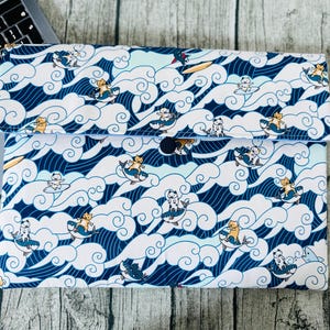 Puede incluir: Una funda para portátil blanca con un patrón de olas azul y blanco y gatos de dibujos animados haciendo surf. Los gatos llevan trajes de baño de diferentes colores y tienen diferentes expresiones.