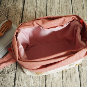 May include: A pink fabric lunch bag with a white lining and a floral pattern. The bag is open and empty.
