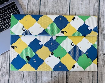 May include: A colorful laptop sleeve with a geometric pattern of yellow, blue, green, and white diamonds. Black cat silhouettes are scattered throughout the design. The sleeve has a flap closure with a white button.