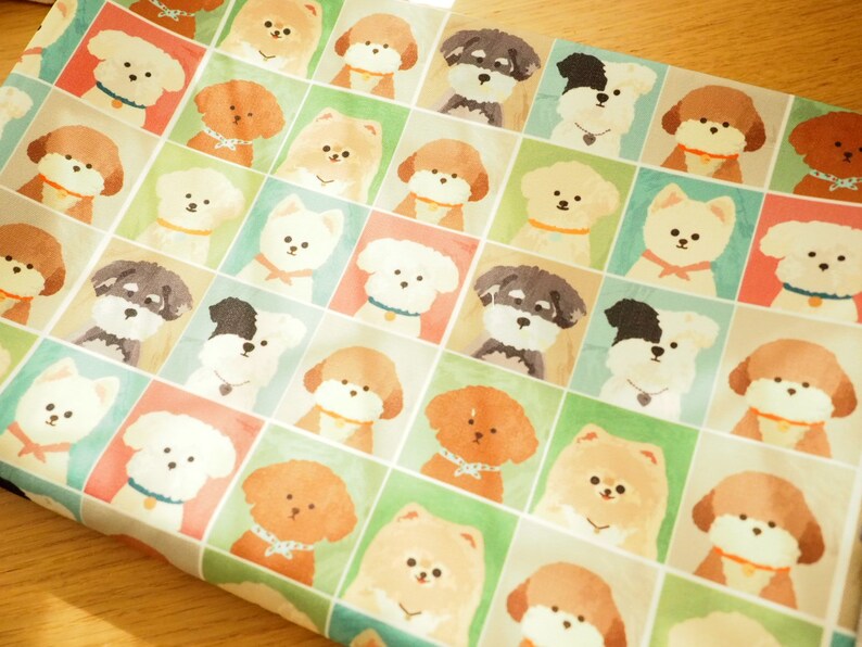 May include: A white fabric with a repeating pattern of various dog breeds in colorful squares. The dogs are illustrated in a cartoon style with different expressions and poses.