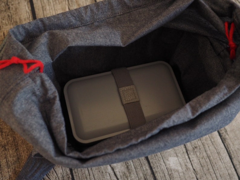 May include: A gray lunch bag with a red drawstring and a gray lunchbox inside.