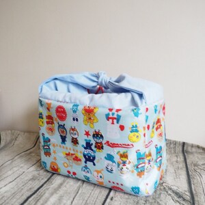 May include: A light blue fabric drawstring bag with a colorful cartoon print featuring characters from the Japanese anime series "Yo-kai Watch".