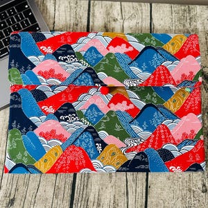 May include: A rectangular fabric pouch featuring a colorful pattern of stylized mountains in shades of red, blue, green, and pink, accented with white wave motifs and floral details. The pouch includes a flap closure secured by a small red button.