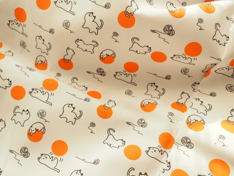 May include: White fabric with a repeating pattern of orange circles and black line drawings of cats playing with yarn.