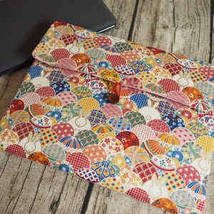 以下が含まれることがあります： 円とウサギのカラフルな日本のパターンが施された白いラップトップスリーブ。スリーブには赤いジッパーと茶色のボタンが付いています。