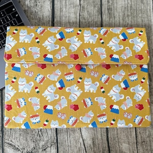 Pode incluir: Capa para laptop amarelo mostarda com um padrão repetido de cães Shiba Inu, Monte Fuji e comida japonesa. A capa tem um fecho de botão vermelho e é feita de tecido.