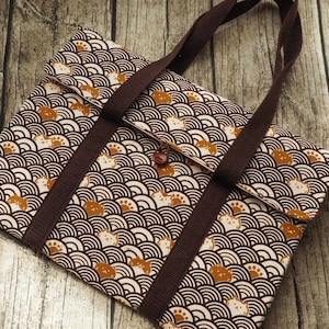 Puede incluir: Una bolsa de mano marrón con un patrón blanco y marrón de olas estilizadas y gatos. La bolsa tiene asas marrones y un cierre de solapa.