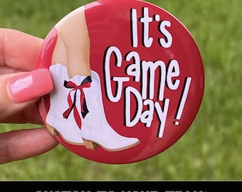 May include: A red button with the text "It's Game Day!" in white. The button features an illustration of white cowboy boots with a red and black bow. The bottom of the button reads "CUSTOM TO YOUR TEAM!"