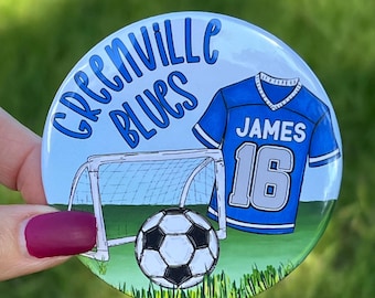 May include: A blue and white soccer jersey with the name "JAMES" and the number "16" on the back. The jersey is in front of a soccer goal and a soccer ball. The text "GREENVILLE BLUES" is at the top of the image.