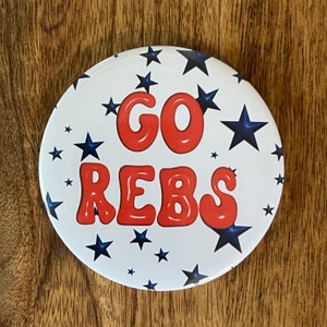 May include: A white button with blue stars and red lettering that says "GO REBS".