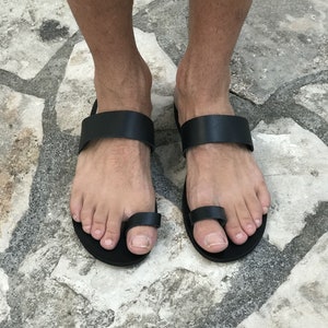 May include: Black leather sandals with a toe loop. The sandals have a simple design and are made of high-quality leather.