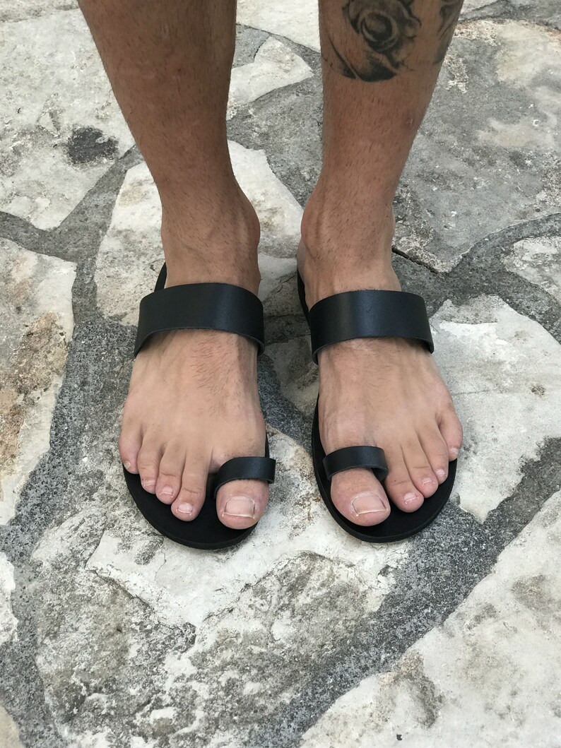 May include: Black leather sandals with a toe loop. The sandals have a simple design and are made of high-quality leather.