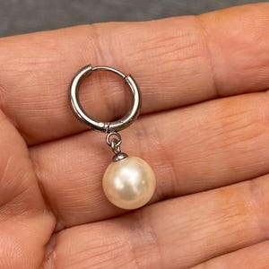 Può includere: Un orecchino a cerchio d'argento con una perla bianca pendente.