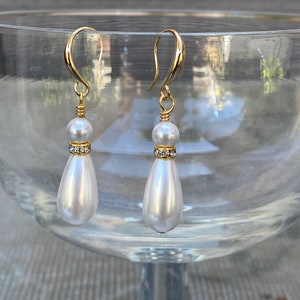 May include: A pair of gold teardrop earrings with a white pearl and a small row of clear rhinestones.