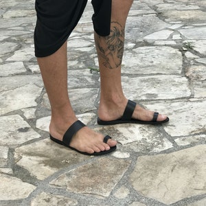 May include: A pair of black leather thong sandals with a simple design. The sandals have a single strap across the foot and a toe loop.