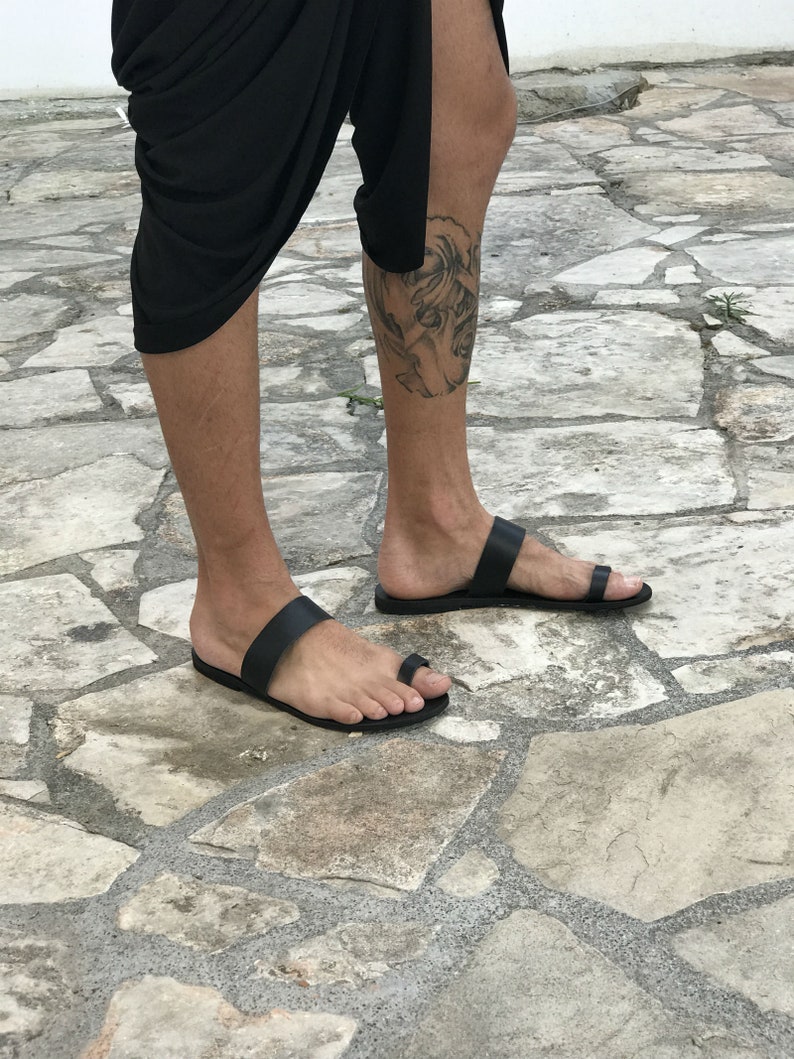May include: A pair of black leather thong sandals with a simple design. The sandals have a single strap across the foot and a toe loop.