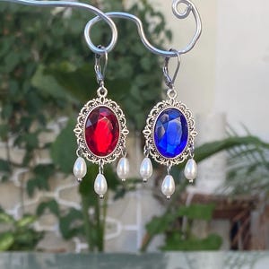 Peut inclure: Une paire de boucles d'oreilles en argent avec une pierre précieuse rouge et bleue, chacune avec une perle pendante.