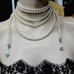 May include: A long, multi-strand pearl necklace with a teardrop-shaped pearl pendant at each end. The necklace is made of white pearls and is worn by a mannequin.