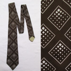 May include: A brown necktie with a repeating pattern of white squares and dots. The tie is displayed on a white background, with a close-up of the fabric pattern on the right side.