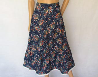 Könnte beinhalten: Ein schwarzes Crop-Top mit herzförmigem Ausschnitt und Knopfdetails, kombiniert mit einem marineblauen Rock mit floralem Muster. Der Rock hat eine weiße Spitzentrimmung am Saum. Das Outfit wird mit schwarzen Sandalen getragen.