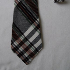 Może przedstawiać: Krawat w kratę o klasycznym wzorze. Krawat ma powtarzający się wzór białych, czarnych, brązowych, zielonych i brzoskwiniowych pasków. Krawat jest prezentowany na białym tle.