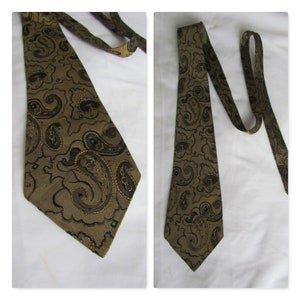 May include: A brown paisley tie featuring a repeating pattern of dark brown and gold paisley shapes. The tie has a pointed end and a green square detail near the tip. The tie is displayed on a white background.