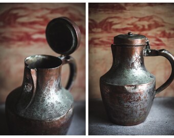 May include: Two images of a vintage copper pitcher with a hinged lid. The pitcher has a handle and a spout. The copper has a patina with areas of green and silver. The background is a faded red and white pattern.