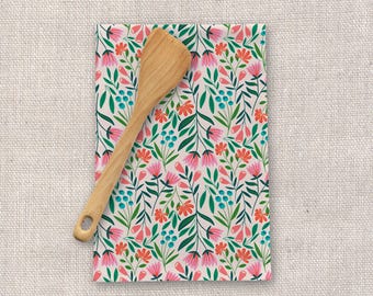 May include: A white kitchen towel with a floral pattern featuring pink, red, and blue flowers on green stems. A wooden spatula is lying on top of the towel.