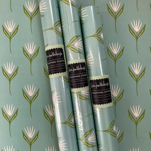 May include: Three rolls of blue wrapping paper with a white floral pattern and the text "Ribbon Jane Workshop Wrapping Paper" printed on each roll.