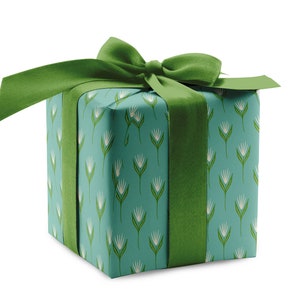 May include: A teal gift box with a green ribbon and a white floral pattern. The box is wrapped in a decorative paper with a repeating pattern of white flowers and green stems.