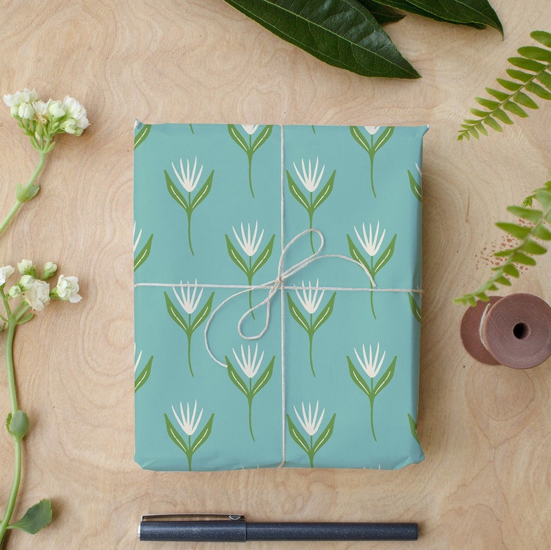 May include: A blue gift box with a white floral pattern wrapped with twine. The box is on a wooden surface.