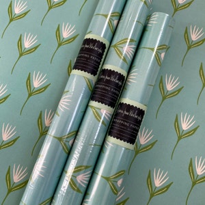 May include: Three rolls of blue and white floral wrapping paper with a green label that reads "Rebecca Jane Worthington Wrapping Paper - 20 x 28 inches - Printed in the USA - www.rebeccajaneworthington.com".