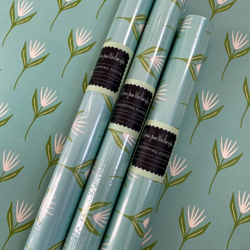 May include: Three rolls of blue and white floral wrapping paper with a green label that reads "Rebecca Jane Worthington Wrapping Paper - 20 x 28 inches - Printed in the USA - www.rebeccajaneworthington.com".