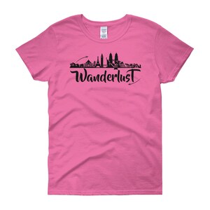May include: Pink women's t-shirt with a black silhouette of a city skyline and the word "Wanderlust" in black script.