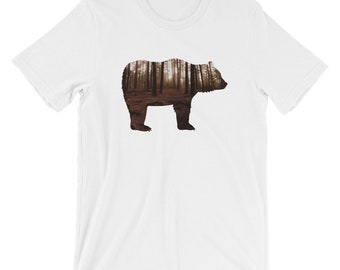 Può includere: Maglietta bianca con la silhouette di un orso. L'orso è riempito con un'immagine di una foresta con alberi e un sentiero.