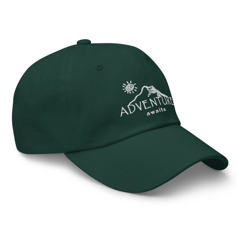 Puede incluir: Una gorra de b&eacute;isbol verde oscuro con un dise&ntilde;o bordado en blanco de una monta&ntilde;a, un sol y el texto "ADVENTURE awaits".