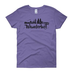 May include: Purple women's t-shirt with a black silhouette of a city skyline and the word "Wanderlust" in black script.