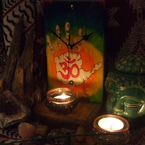 May include: A wooden clock with a handprint design and the symbol Om painted on it. The clock is surrounded by candles, crystals, and incense.